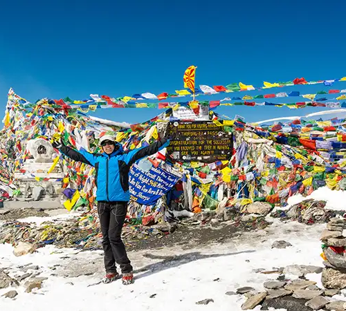 A line of trekkers crossing a high-altitude mountain pass decorated with thousands of colorful Buddhist prayer flags during an Annapurna Circuit Trek.