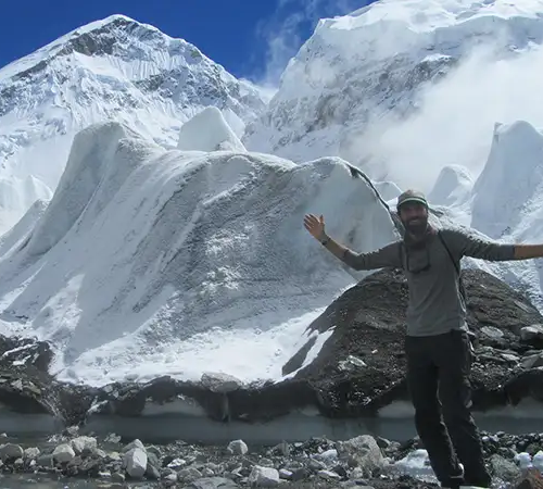 A stone cairn stands on a snowy ridge overlooking a frozen turquoise lake and a remote mountain village during an Everest Three Passes Trek.