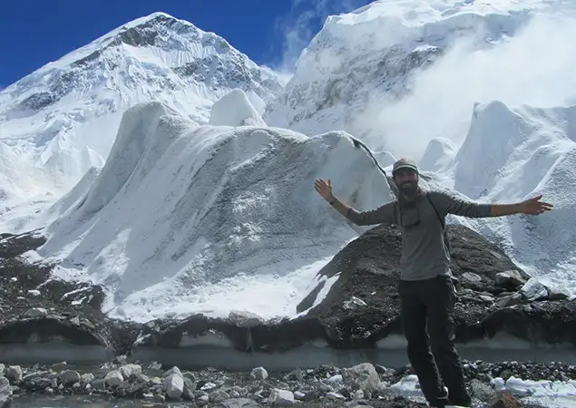 A stone cairn stands on a snowy ridge overlooking a frozen turquoise lake and a remote mountain village during an Everest Three Passes Trek.