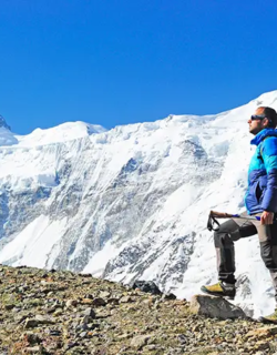 A hiker wearing a bright green down jacket and a grey backpack uses trekking poles to climb a steep snow covered slope during an Everest Base Camp Trek for beginners.