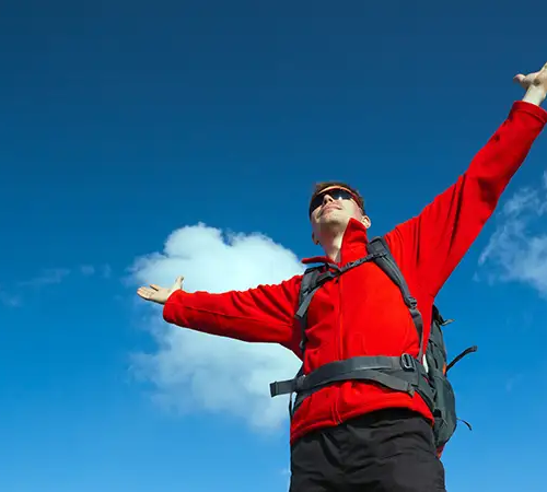 Beginner trekker celebrating success on the Annapurna Base Camp trek with arms outstretched under clear Himalayan skies.