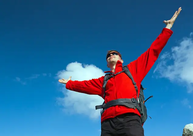 Beginner trekker celebrating success on the Annapurna Base Camp trek with arms outstretched under clear Himalayan skies.