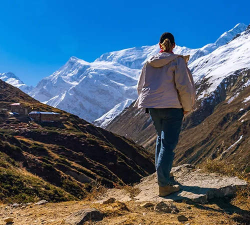 A hiker stands on a rock, taking in the grand view of massive snow-capped mountains and a winding valley, illustrating the beautiful rewards of an Annapurna Base Camp Trek for Beginners.