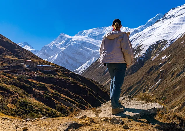 A hiker stands on a rock, taking in the grand view of massive snow-capped mountains and a winding valley, illustrating the beautiful rewards of an Annapurna Base Camp Trek for Beginners.