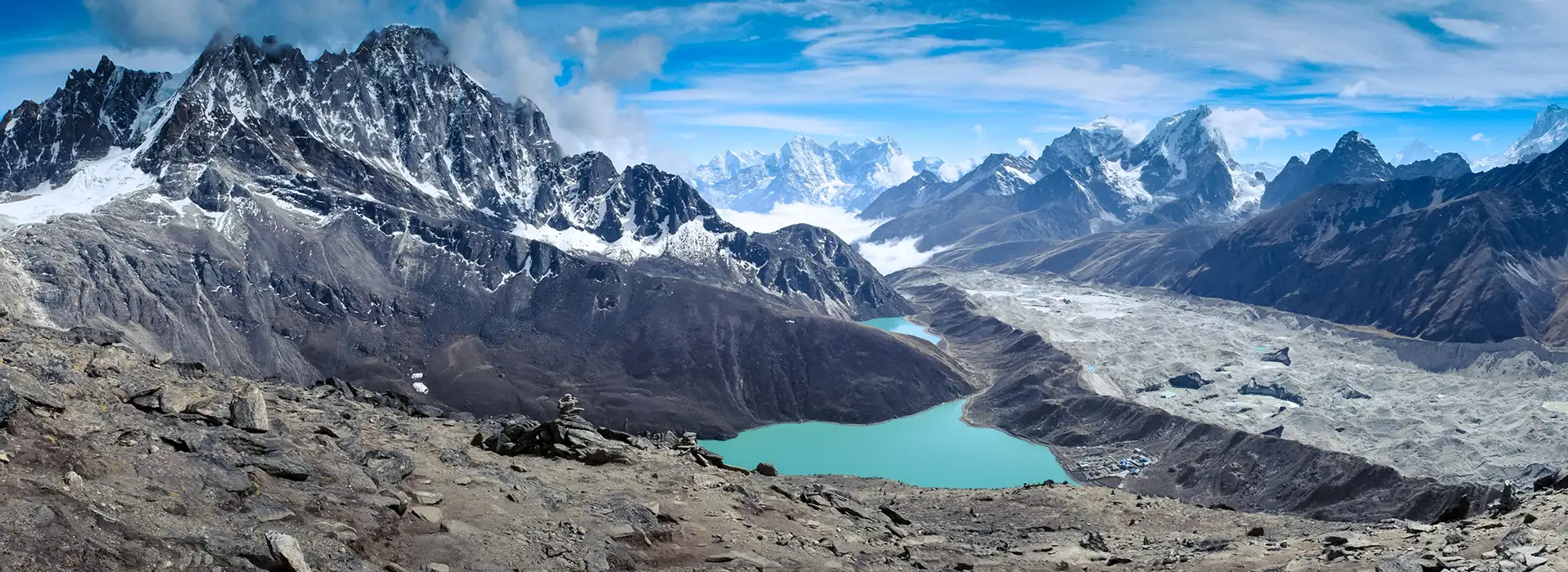 A wide panorama shows a bright turquoise lake at the edge of the rocky Ngozumpa Glacier, with towering snowy peaks in the distance, a key landscape on the Gokyo Lake Everest Base Camp Trek.