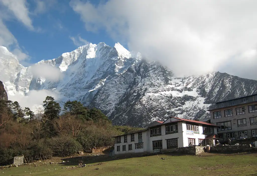 A white two-story mountain lodge with a red roof sits in a grassy valley in Everest Base Camp.