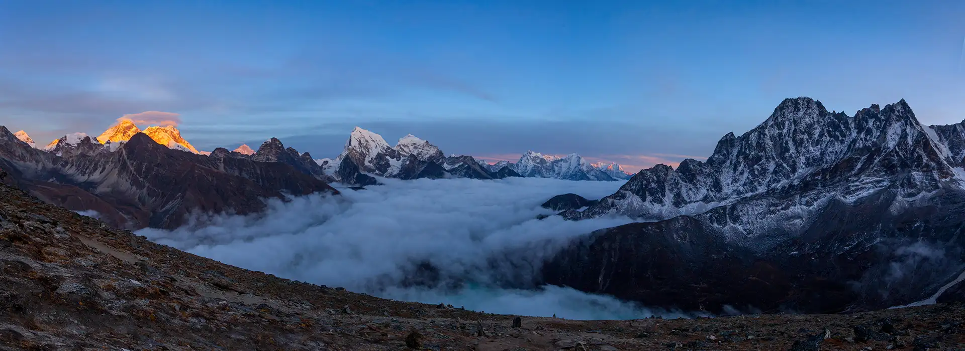 A panoramic view of the Himalayan peaks at sunset with a thick layer of clouds filling the valley below, captured during a Gokyo Trek.