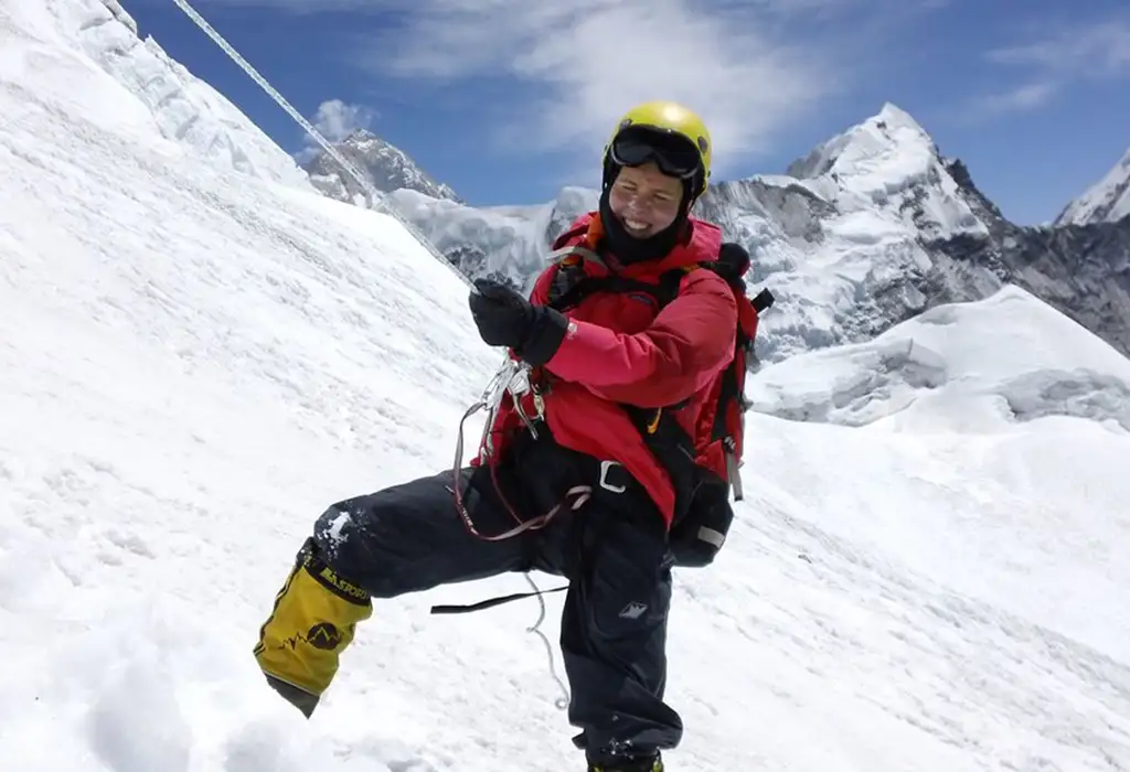A smiling mountaineer in a red jacket and yellow helmet uses a jumar and fixed rope during an Island Peak climbing expedition.