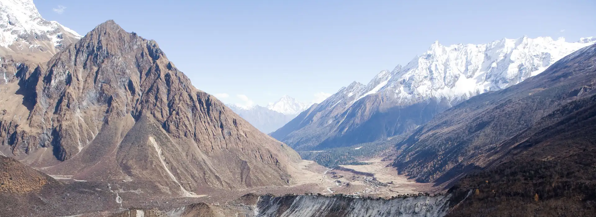 A wide panoramic landscape of a deep mountain valley in the Himalayas, showing snowy peaks and rugged terrain of Manaslu Circuit Trek