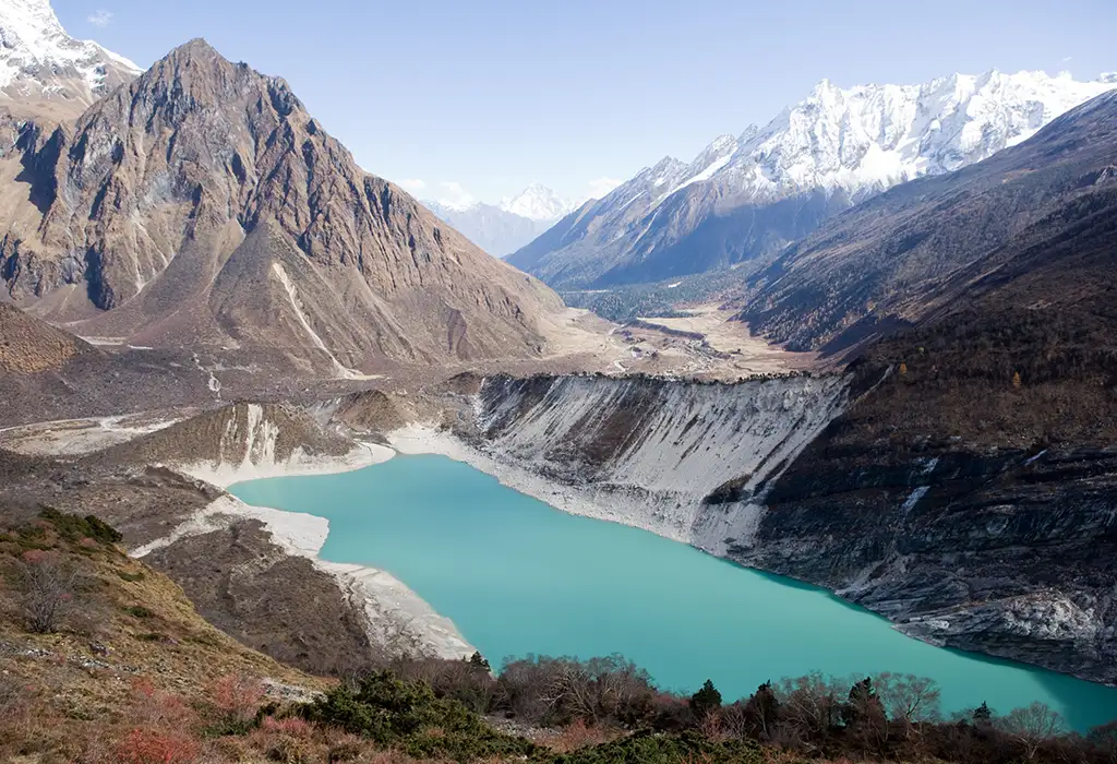 A wide shot of a bright turquoise glacial lake nestled in a Manaslu region seen during Manaslu Circuit Trek.