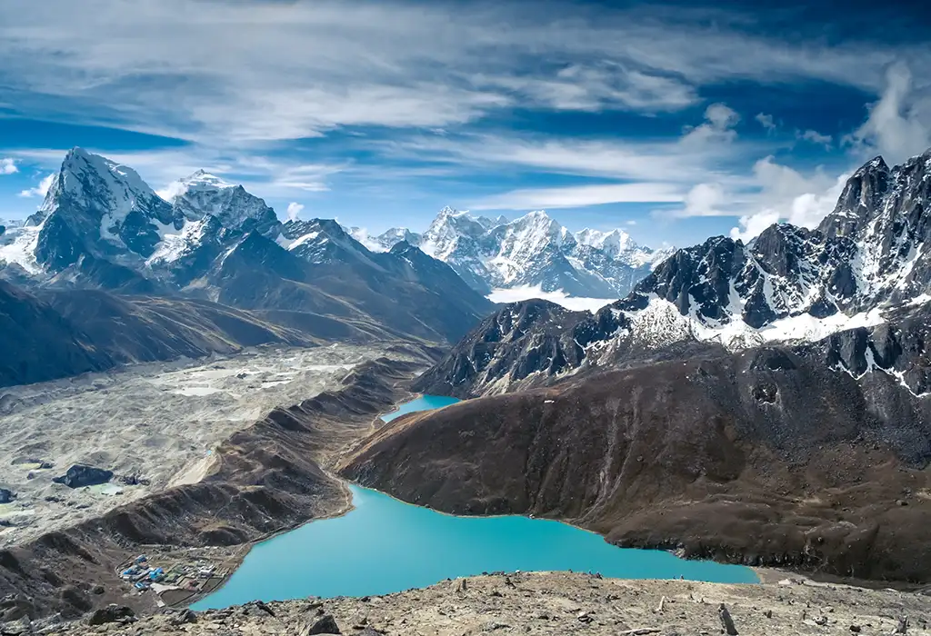 A high-altitude view of a brilliant turquoise lake nestled beside the massive, debris-covered Ngozumpa Glacier, a highlight of the Gokyo Trek in Nepal.