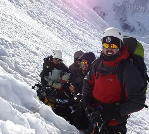 A group of four mountaineers in helmets and sunglasses take a break on a steep, icy incline during an Island peak climbing expedition.