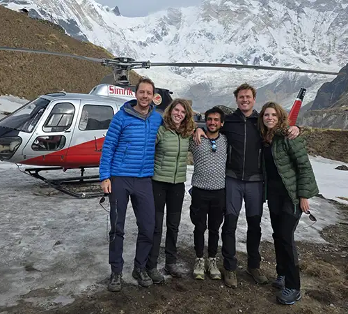 A group of five people in hiking gear stands together for a photo on a snowy mountain patch during a Luxury Sherpa Village Hike with Everest Helicopter Tour