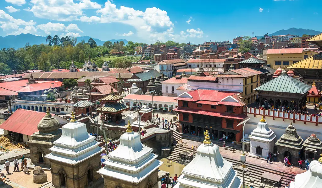 An aerial view of the historic Pashupatinath Temple complex in Kathmandu with traditional red-roofed buildings and white stone stupas.