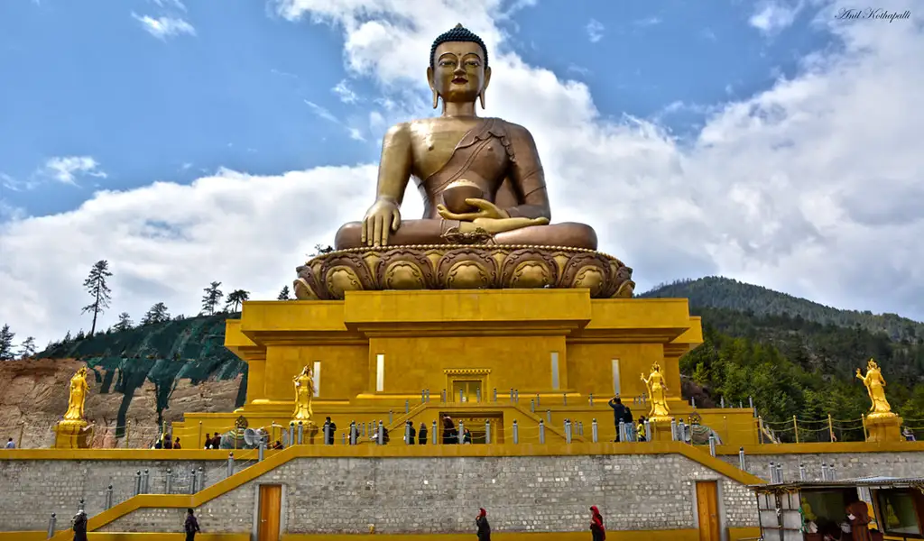 The 51-meter-tall Buddha Dordenma statue overlooking Thimphu Valley, Bhutan, set against forested hills and a partly cloudy sky as seen in Thimphu travel guide.