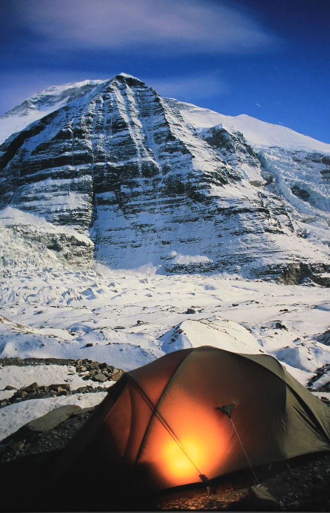 A glowing tent beneath the towering north face of Mount Dhaulagiri at Dhaulagiri Base Camp.Title: Dhaulagiri Base Camp at Night