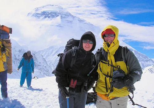 Trekkers and porters on a snowy mountain trail with Mount Dhaulagiri towering in the background during Dhaulagiri Circuit Trek