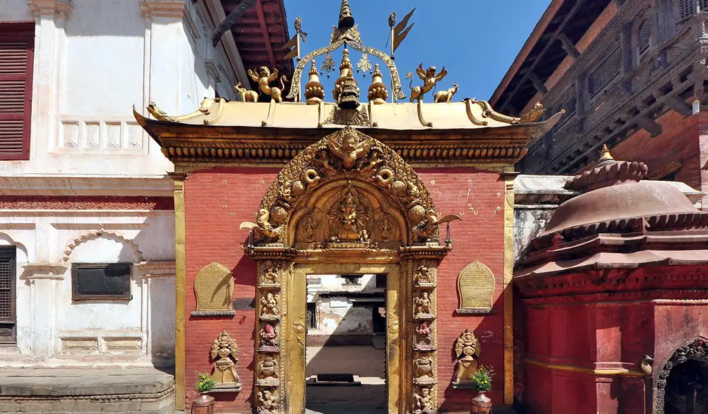 An ornate golden gateway with intricate carvings stands against red brick walls in a historic courtyard.