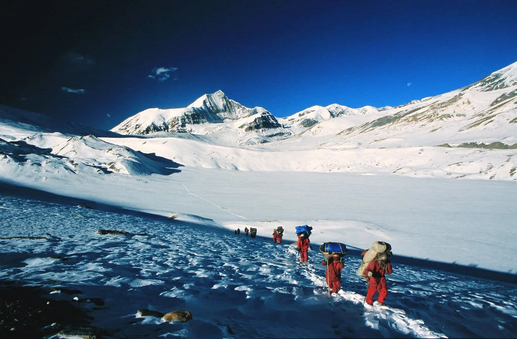 Trekkers crossing Hidden Valley surrounded by snow-covered mountains under a deep blue sky during the Dhaulagiri Circuit Trek.