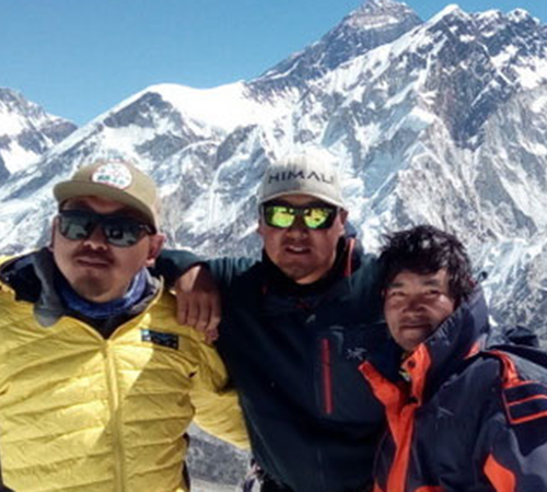 Three climbers standing together near Lobuche Peak, with snow-covered Himalayan mountains rising sharply in the background.