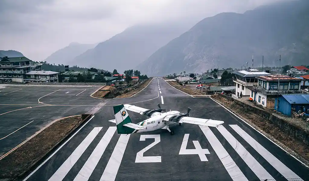 Small aircraft parked on the runway at Lukla Airport, with steep Himalayan mountains and village buildings surrounding the airstrip.