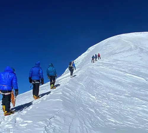 Climbers ascending the snowy ridge of Mera Peak Climbing under a clear blue sky in the Himalayas.