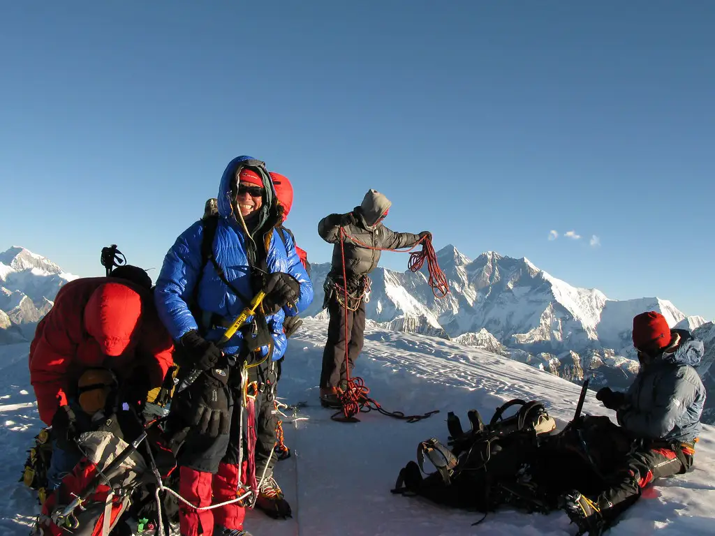 Climbers preparing ropes and gear on the snowy summit ridge of Mera Peak with Himalayan peaks behind.