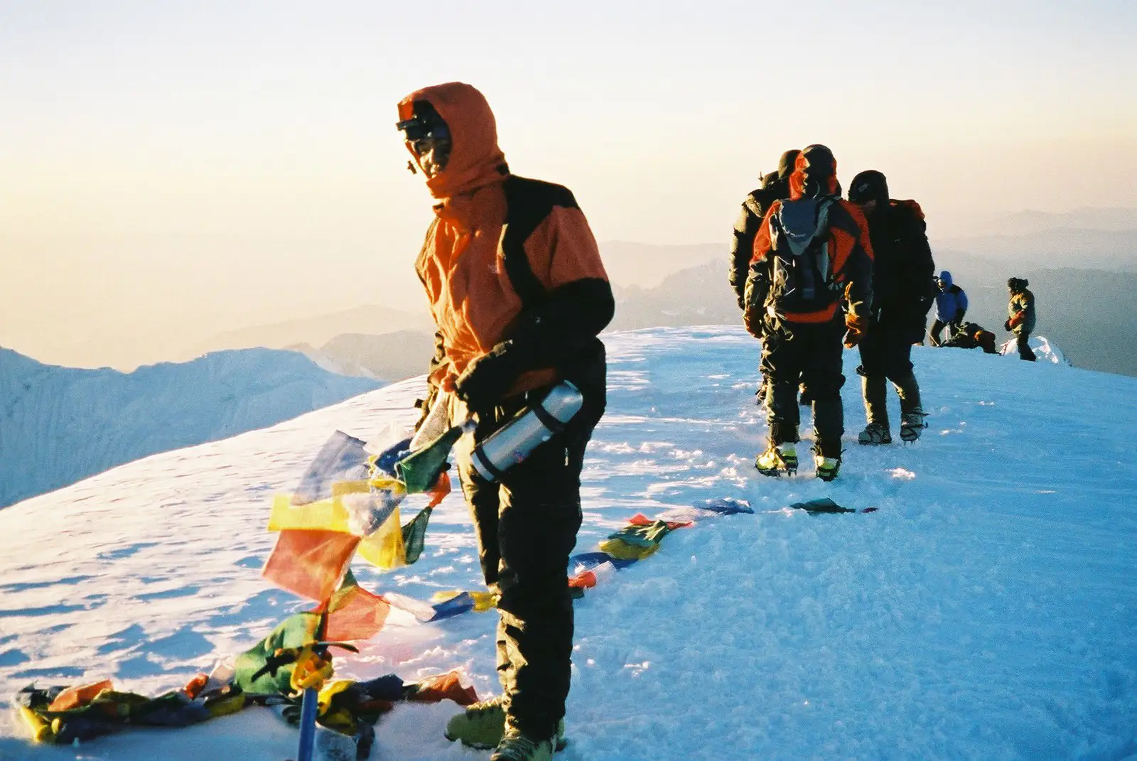 Climbers on the snowy summit of Mera Peak with colorful prayer flags under golden morning light.Title: Sunrise at the Summit of Mera Peak