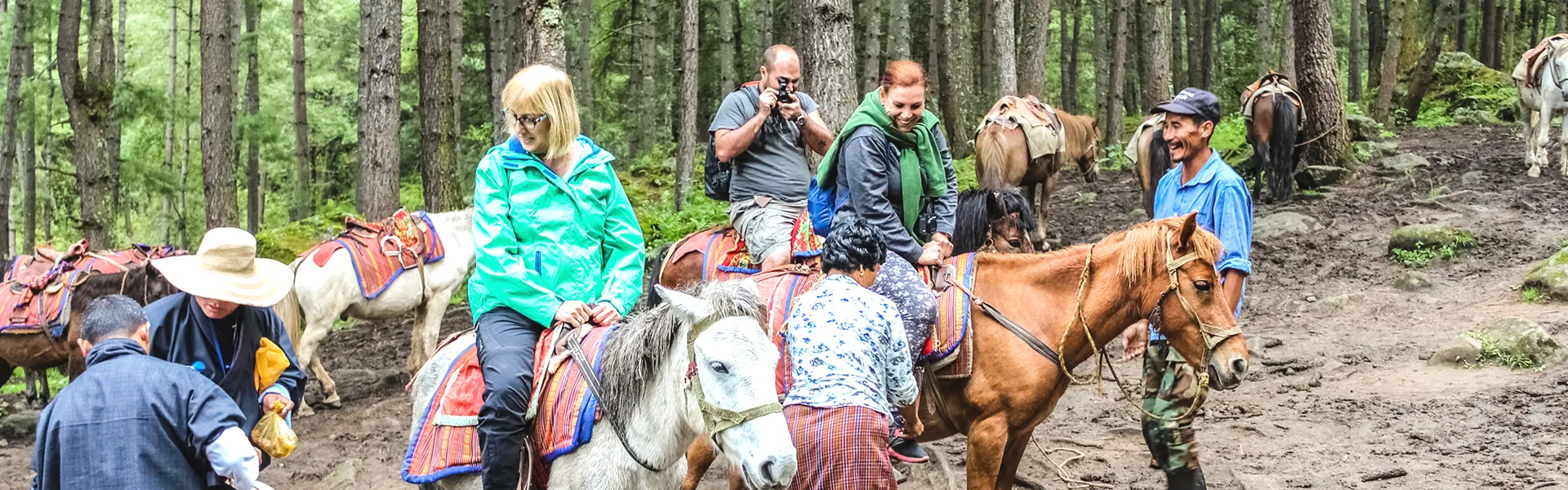 Tourists riding ponies through a lush forest trail toward Tiger’s Nest Monastery in Bhutan, assisted by local guides.
