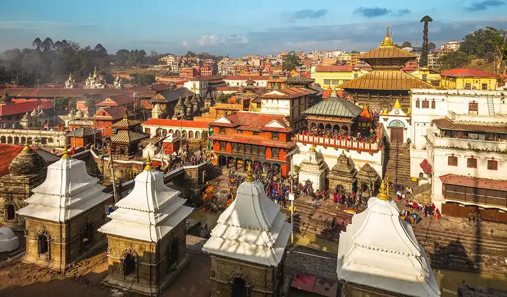Pashupatinath Temple complex in Kathmandu, Nepal, with white cremation platforms along the Bagmati River and surrounding shrines and rooftops.