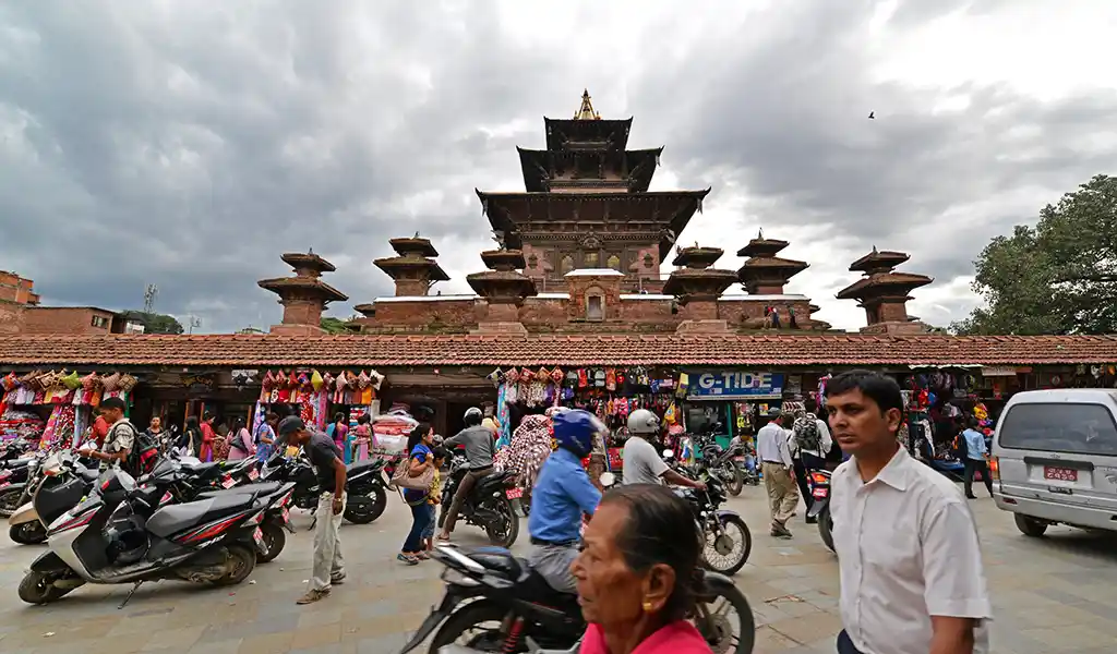 Taleju Bhawani Temple in Kathmandu Durbar Square, Nepal, rising above a busy market area with visitors, motorcycles, and shops in the foreground.