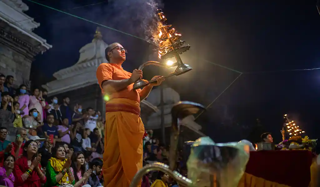 A Hindu priest performs evening aarti with a multi-tiered oil lamp at Pashupatinath Temple in Kathmandu, Nepal, as devotees watch at night during the Nepal and Bhutan Tour