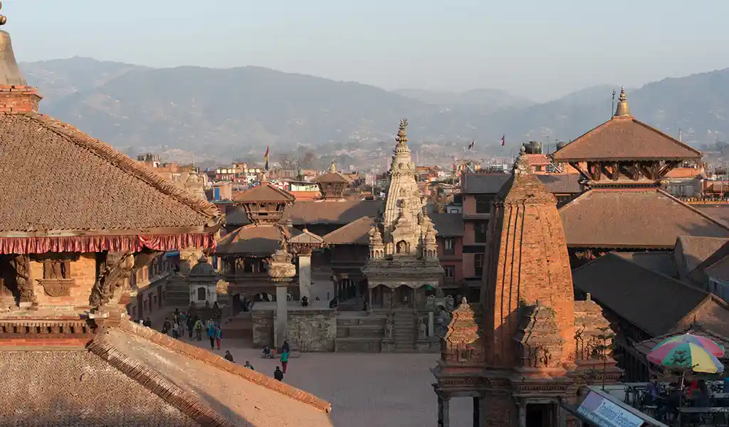 A historic square filled with temples and traditional brick buildings, with hills visible in the background.