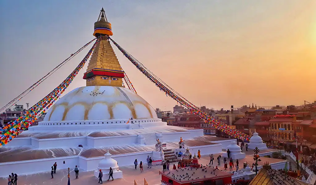 Boudhanath Stupa in Kathmandu, Nepal, decorated with colorful prayer flags during sunset with visitors walking around the stupa.