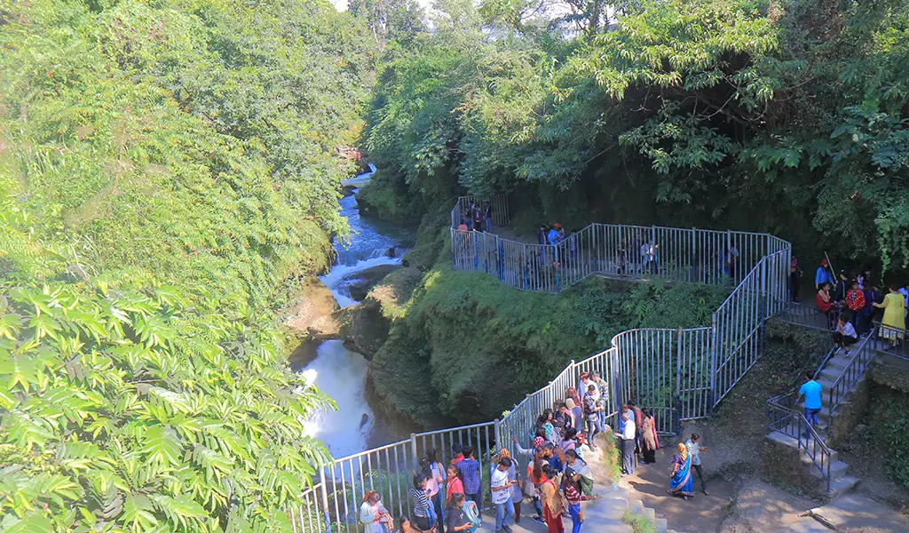 Visitors at Devi’s Falls in Pokhara, Nepal, viewing a powerful waterfall flowing through a narrow gorge surrounded by lush green forest.