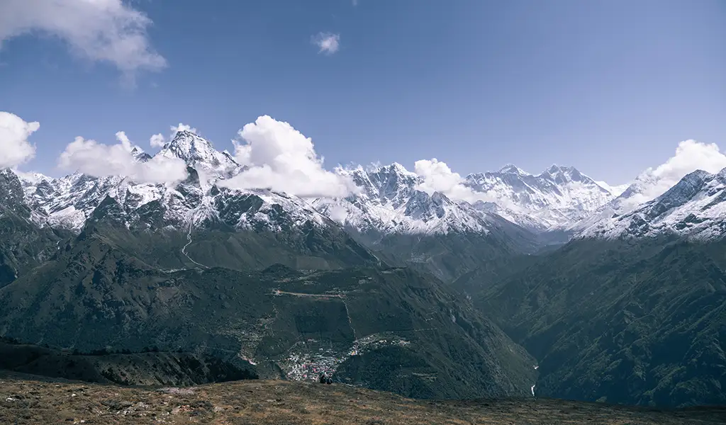 Wide view of Dingboche village set in a high Himalayan valley, surrounded by snow-covered peaks and steep mountain ridges.