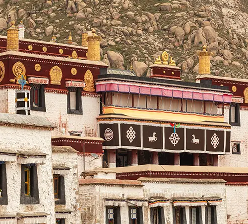 A Tibetan Buddhist monastery complex with whitewashed walls, ornate gold details, and symbolic decorations set against a rocky hillside.