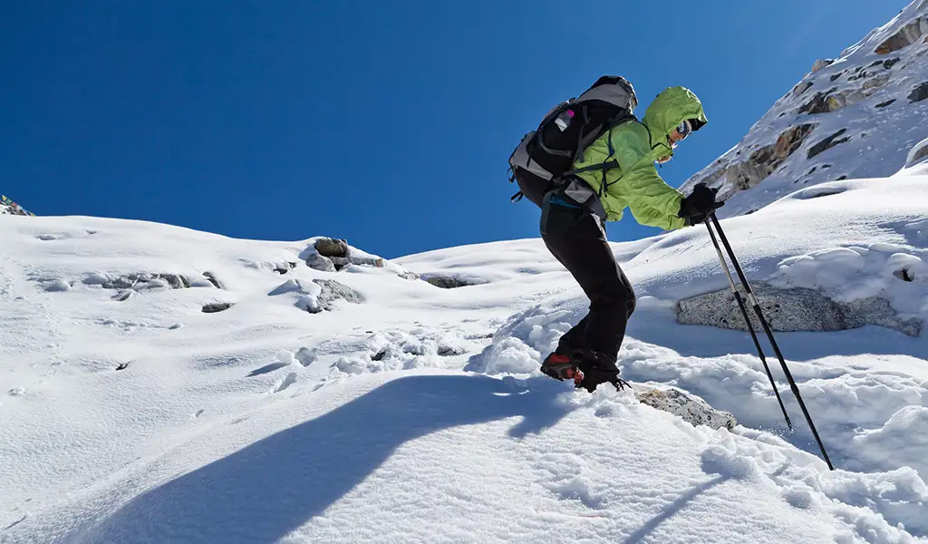 Trekker climbing a snow-covered slope with trekking poles and a backpack in the Everest region, highlighting the Everest Base Camp trek distance.