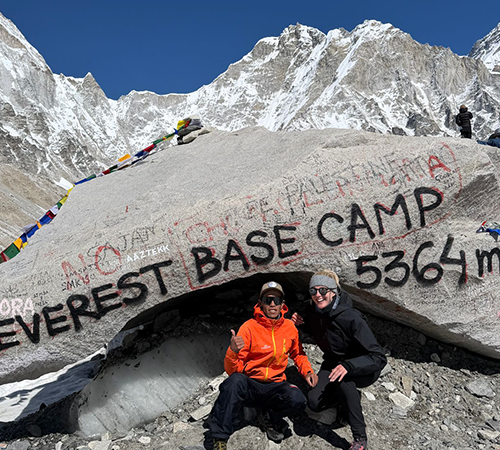 Two trekkers posing beside the Everest Base Camp rock marked 5,364 meters, with surrounding glaciers and high-altitude terrain, often referenced when planning everest base camp trek cost.