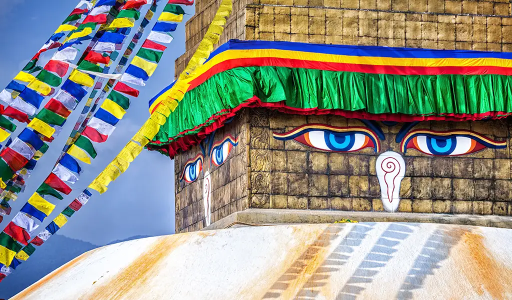 Close-up of the Buddha eyes on Boudhanath Stupa in Kathmandu, Nepal, with colorful prayer flags and a green canopy around the upper tower.