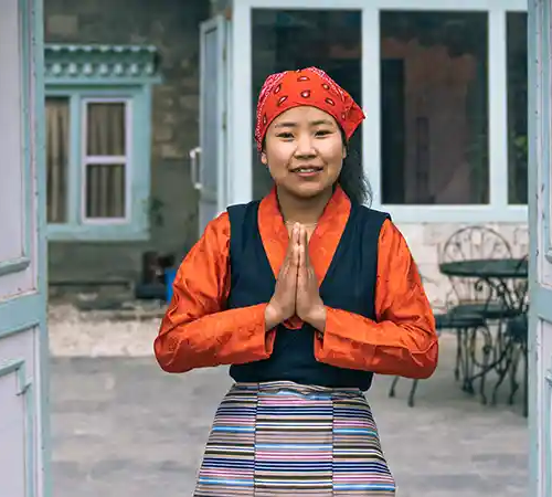 A woman in traditional attire stands with hands pressed together in a Namaste greeting in Namche Bazaar.