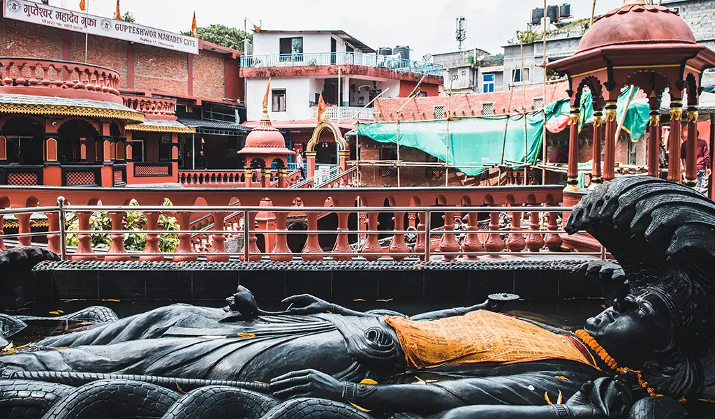Reclining statue of Lord Vishnu at the entrance area of Gupteshwor Mahadev Cave in Pokhara, Nepal, with temple structures and railings in the background.