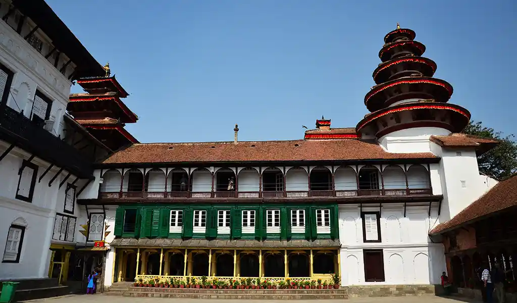 A courtyard view inside Hanuman Dhoka Palace in Kathmandu, Nepal, showing traditional white buildings with green windows and multi-tiered pagoda towers.