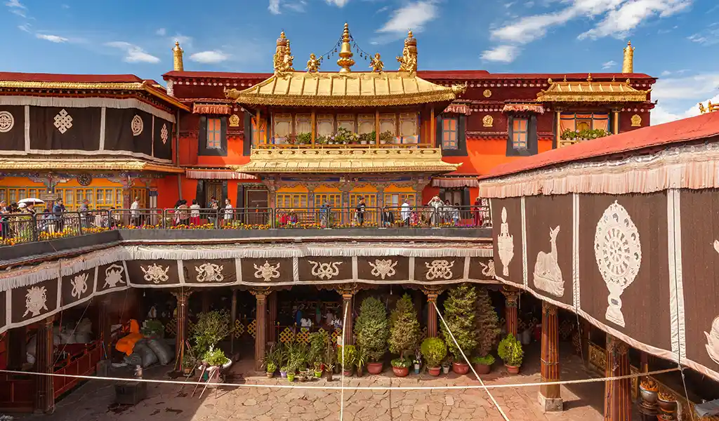 Courtyard of Jokhang Temple in Lhasa, Tibet, with a golden-roofed shrine, red walls, and traditional Tibetan decorative paintings.