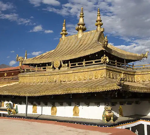 An ornate Buddhist temple with a golden roof and decorative details, set against a blue sky with scattered clouds.