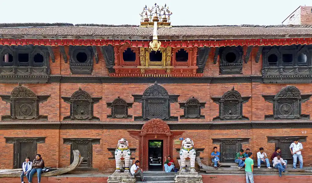 The Kumari Ghar in Kathmandu Durbar Square, Nepal, with red-brick Newar architecture, carved wooden windows, and guardian lion statues at the entrance.