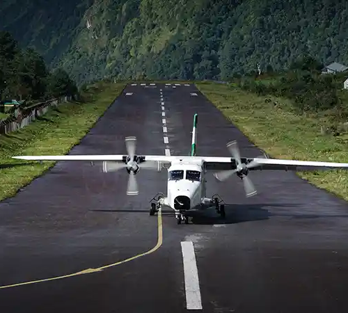 Small aircraft taxiing on the short runway at Lukla Airport, surrounded by steep green hills in the Everest region.