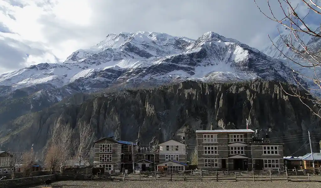 Manang village in Nepal’s Annapurna region with stone buildings beneath snow-capped Himalayan peaks and a steep mountain ridge.