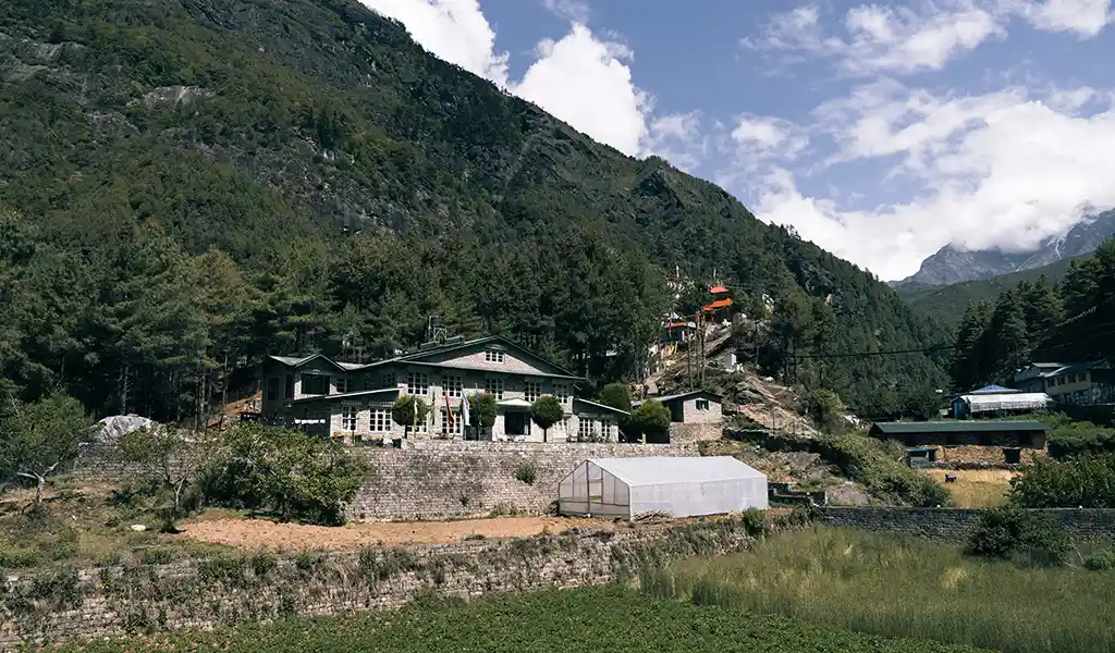 Monjo village with stone lodges and cultivated fields set against forested hills along the Everest Base Camp trekking route.