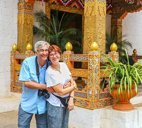 A smiling couple stands in front of an ornate Himalayan monastery courtyard, enjoying a relaxed cultural moment on a Nepal and Bhutan tour surrounded by traditional architecture and vibrant details.